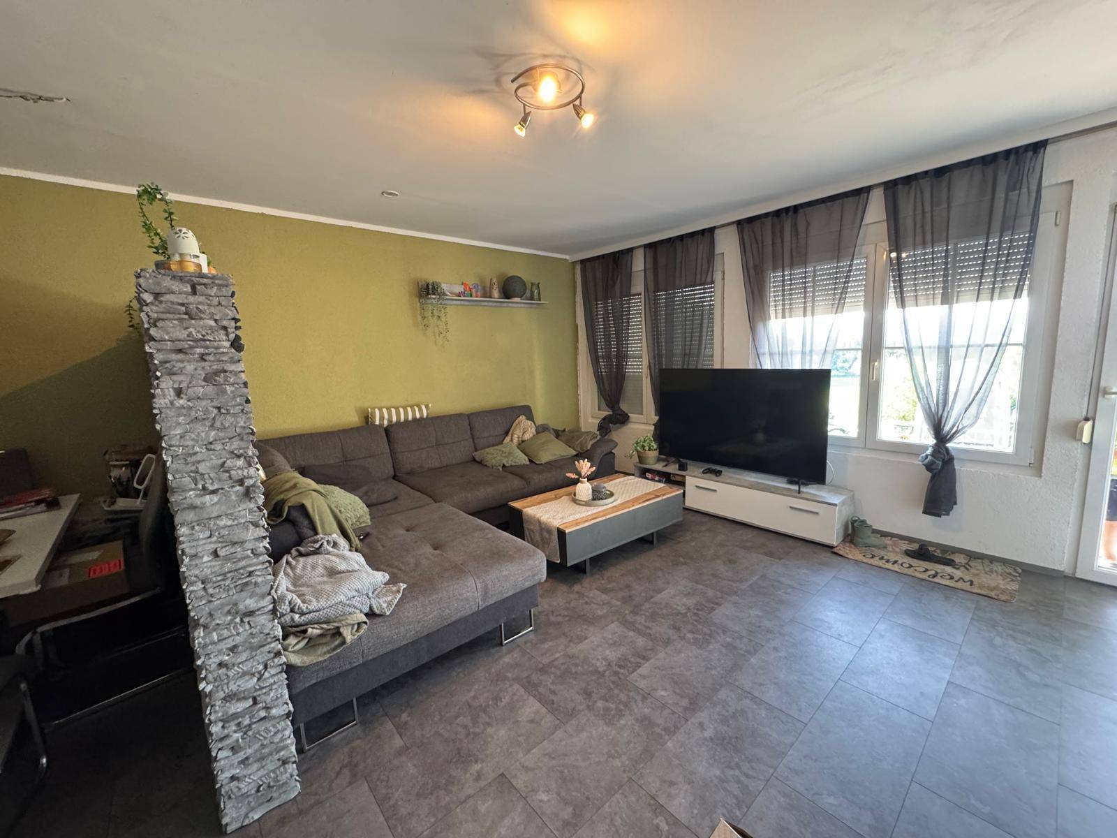 Gemütliches Wohnzimmer mit großem Ecksofa, Fernseher und einer dekorativen Steinwand.