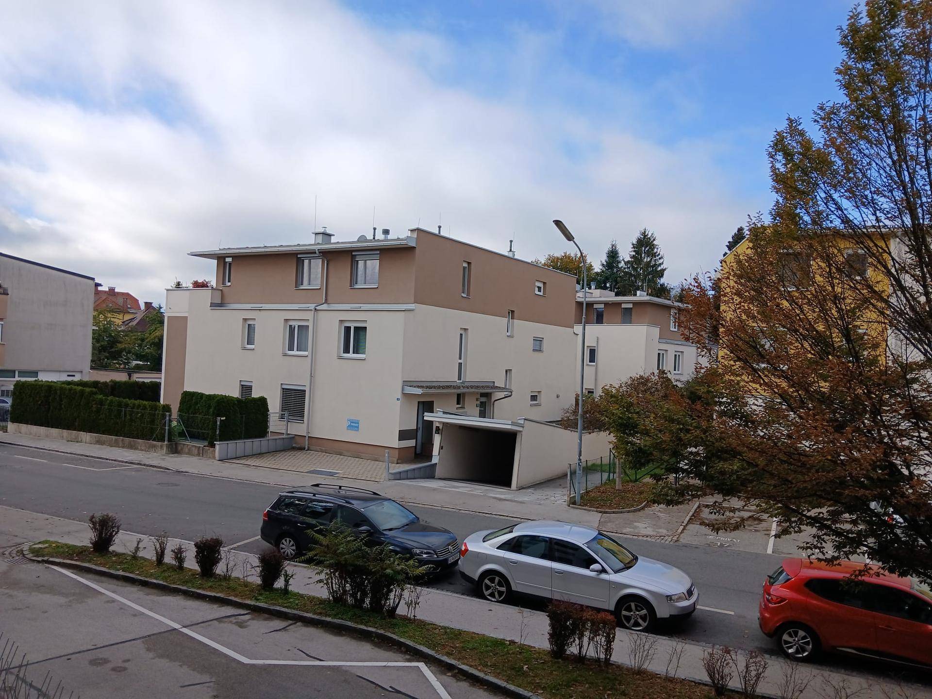 Modernes Mehrfamilienhaus mit beiger und weißer Fassade, Parkplätzen und Bäumen. Die Architektur ist zeitgemäß.