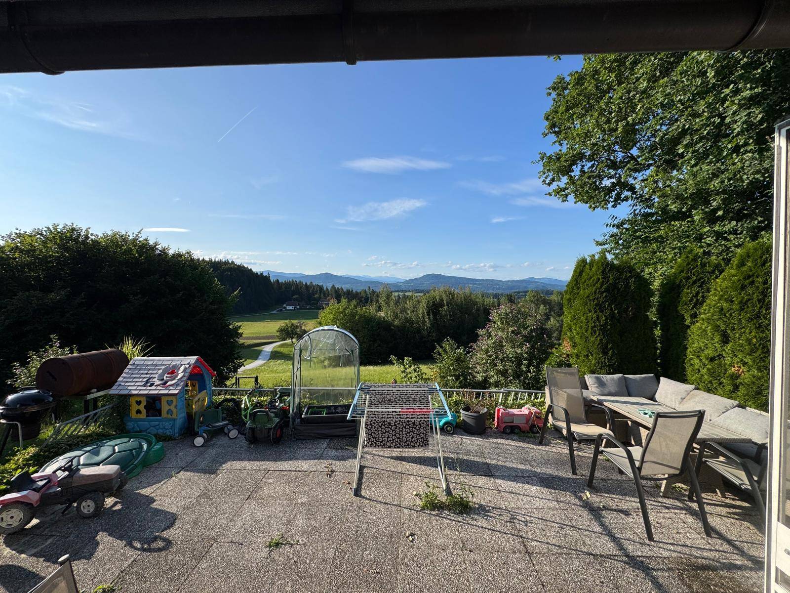 Große Terrasse mit Gartenmöbeln und einem weiten Panoramablick über die grüne Landschaft.