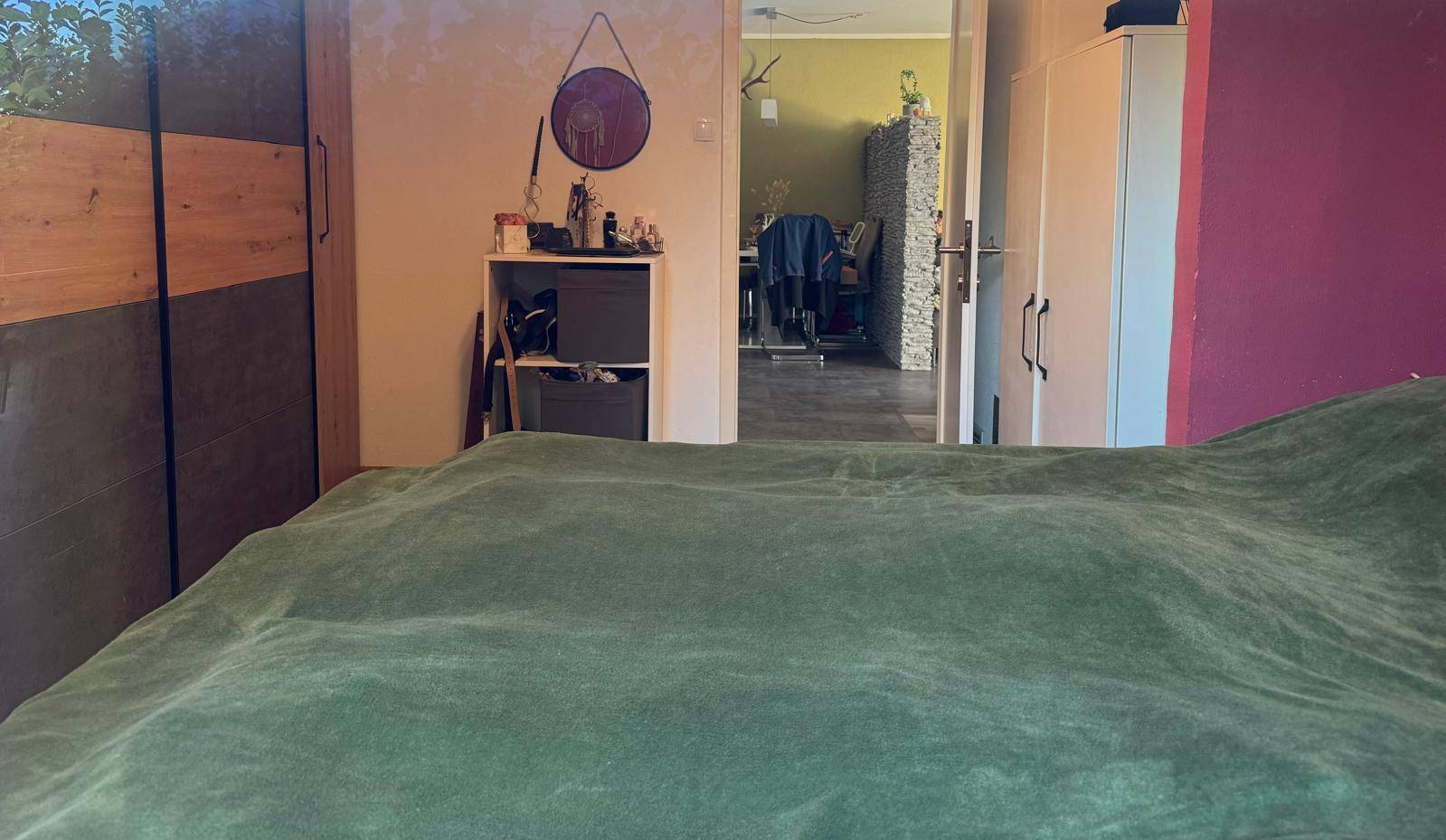 Blick vom Bett im Schlafzimmer in den angrenzenden Wohnbereich mit Laminatboden.