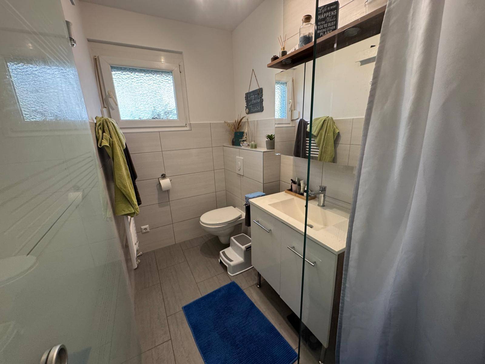 Helles Badezimmer mit modernen Fliesen, Einzelwaschbecken und einer Duschkabine.