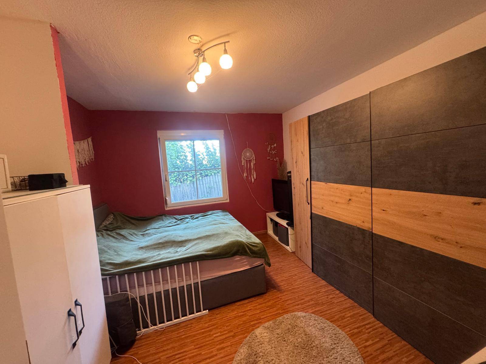 Schlafzimmer mit Fenster, großem Kleiderschrank und Laminatboden, hell und funktional.