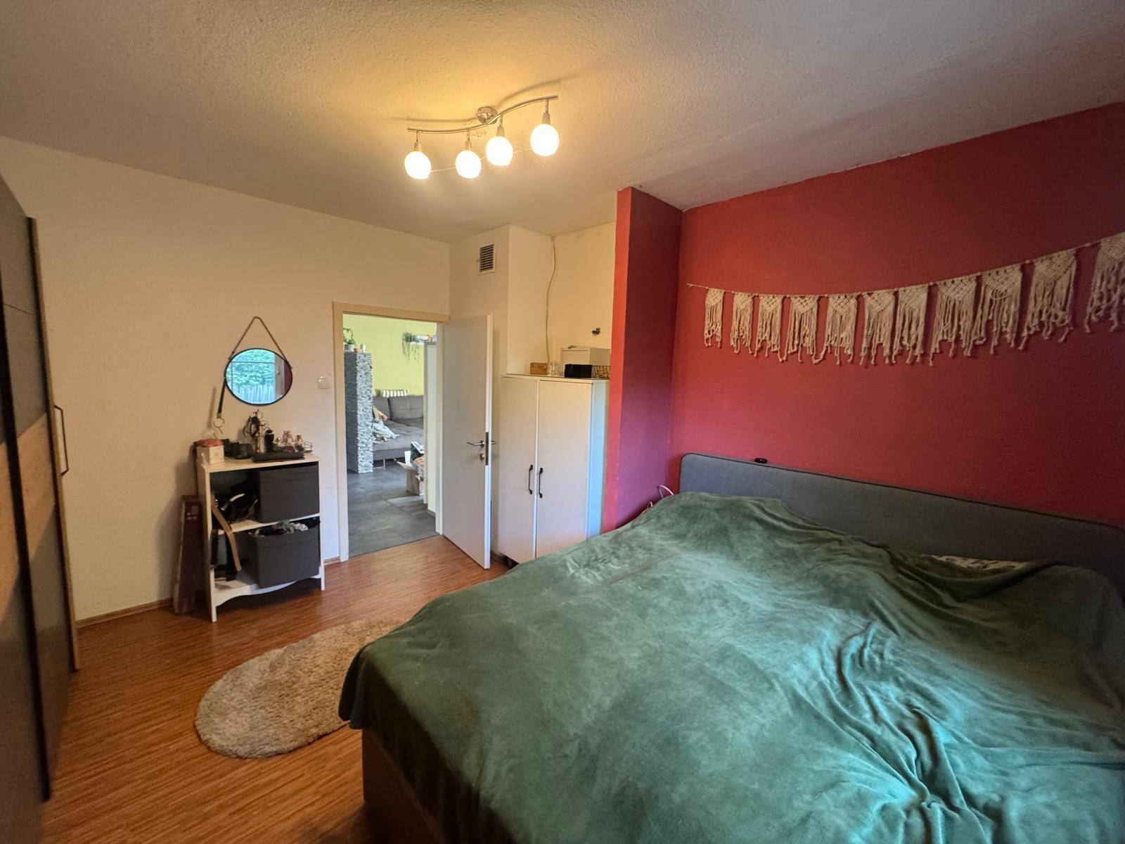 Gemütliches Schlafzimmer mit roter Akzentwand, großem Bett und Laminatboden.