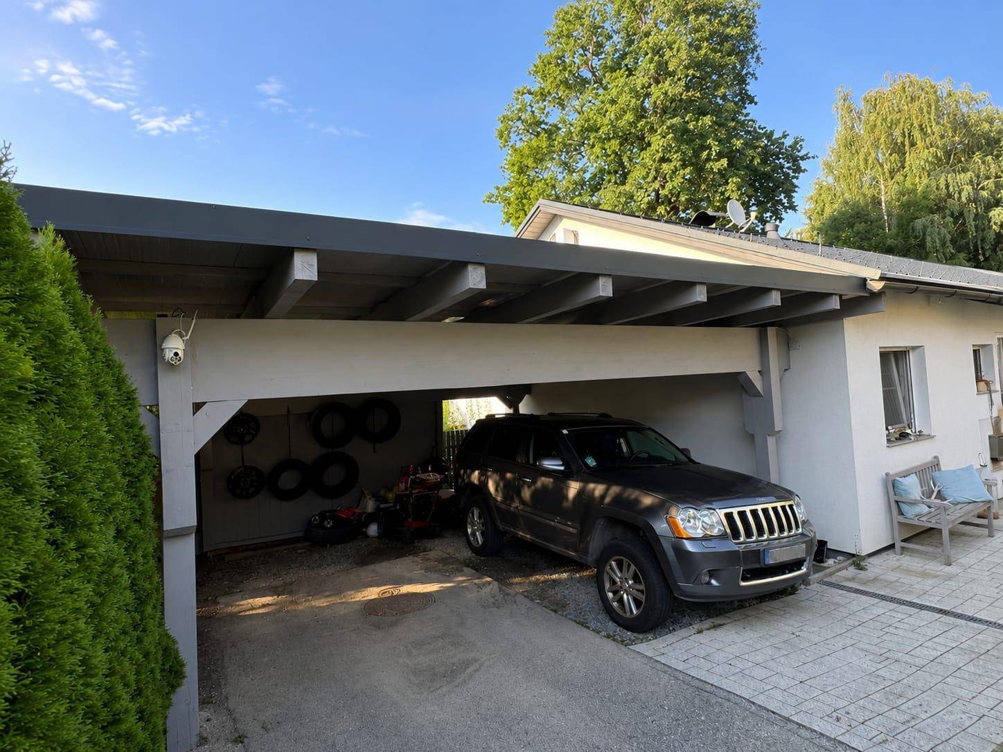 Geräumiger Carport mit einem geparkten SUV und Stauraum für Reifen und Gartengeräte.