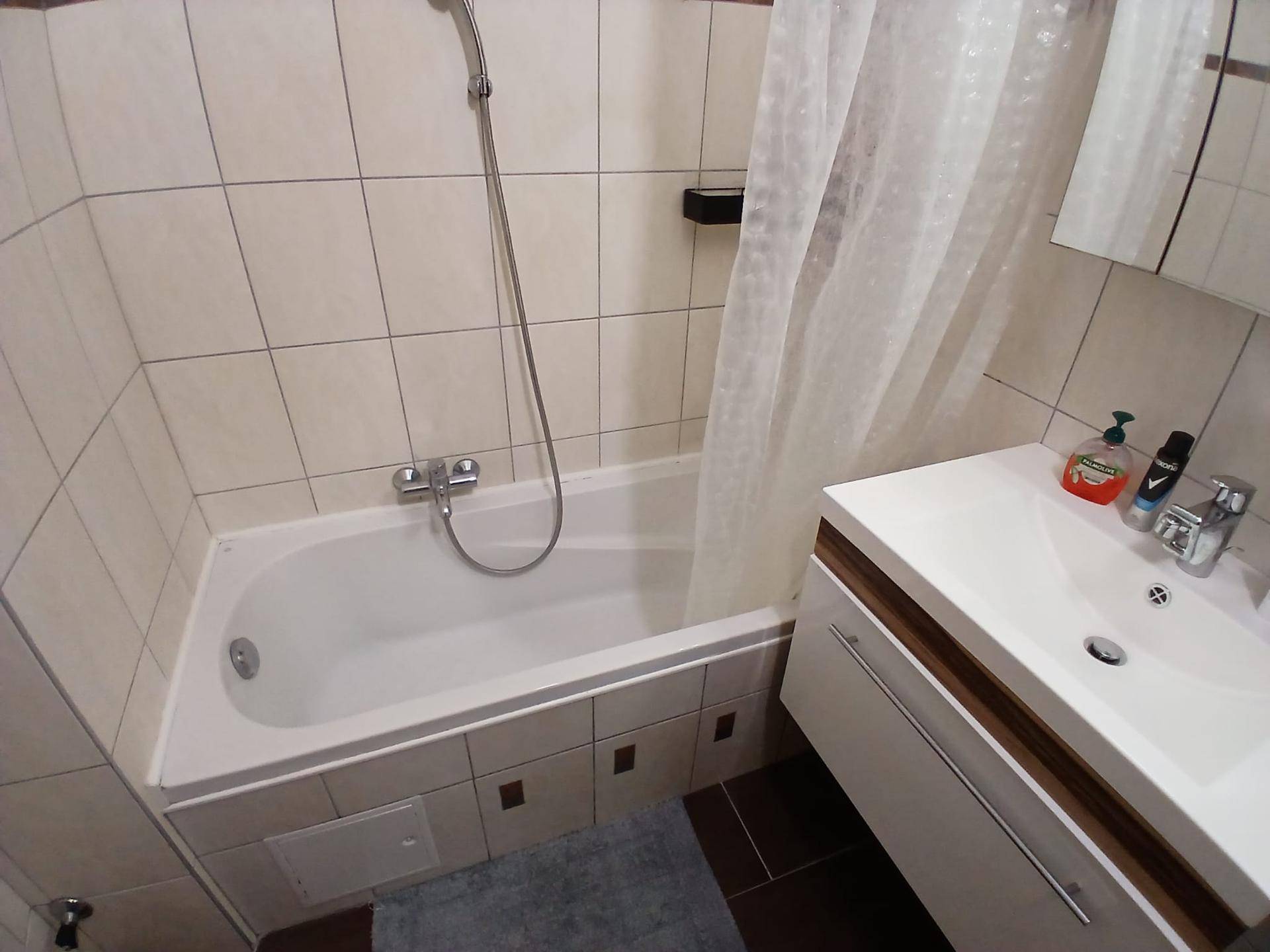 Badezimmer mit Badewanne, Duschvorhang und einem modernen Waschtisch. Die Fliesen sind hell und sauber.