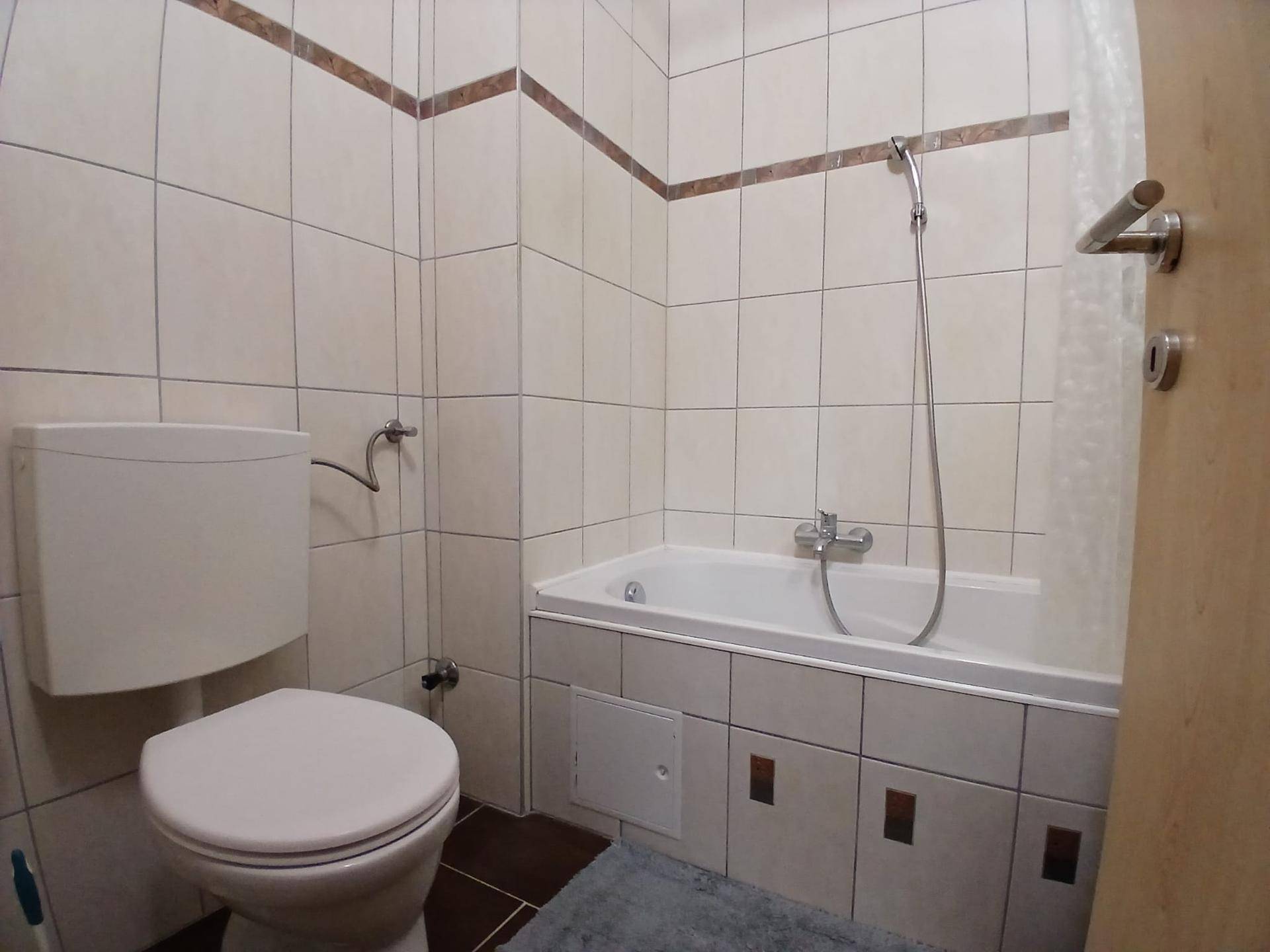 Badezimmer mit Badewanne, Toilette und hellen Wandfliesen. Ein funktionaler Raum mit einfacher Ausstattung.