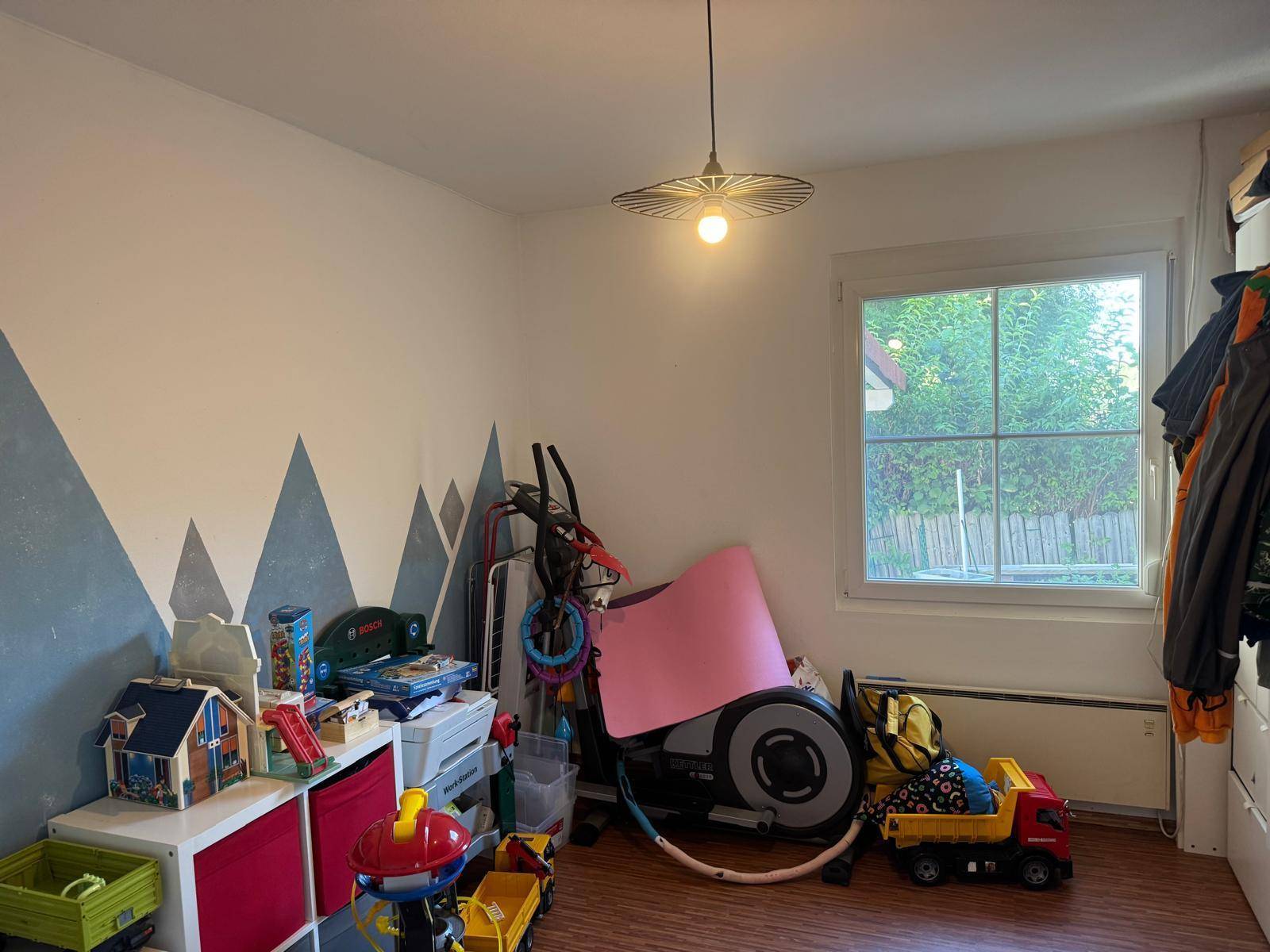 Kinderzimmer mit Fenster, Spielzeug und einer Sportgeräteecke.