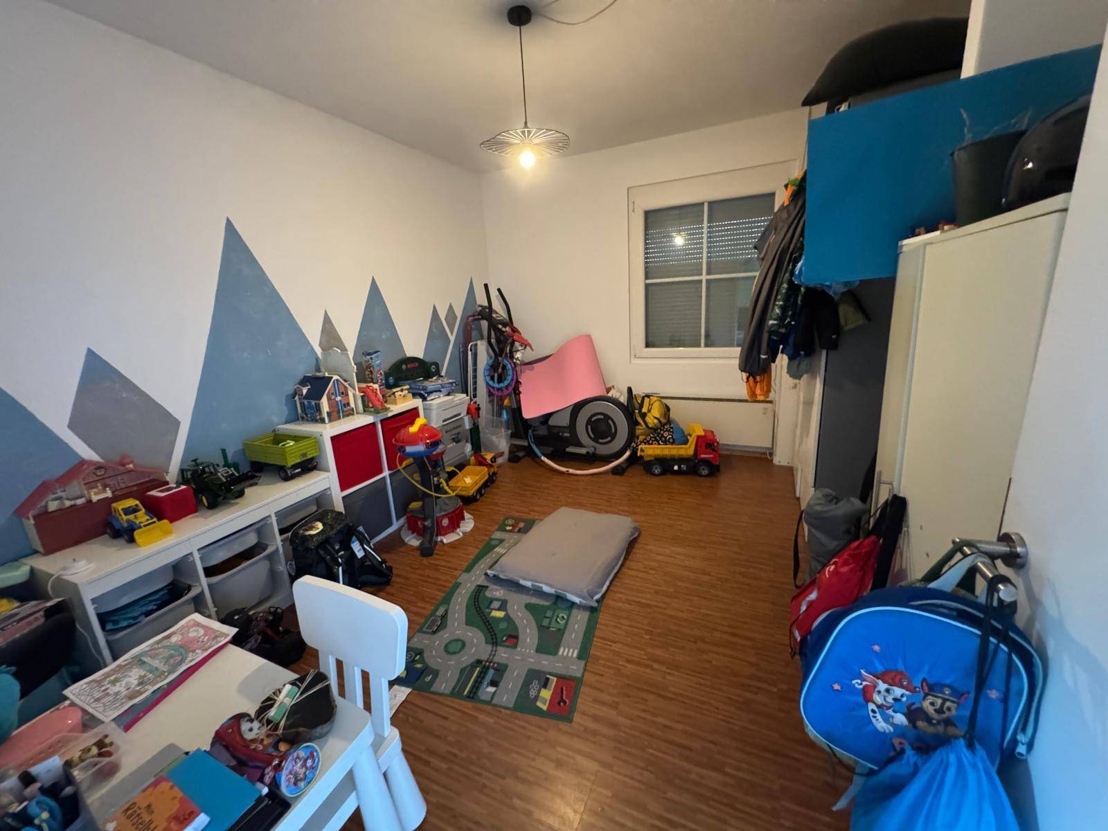 Helles Kinderzimmer mit Spielzeug, Fenster und kreativer Wandgestaltung.