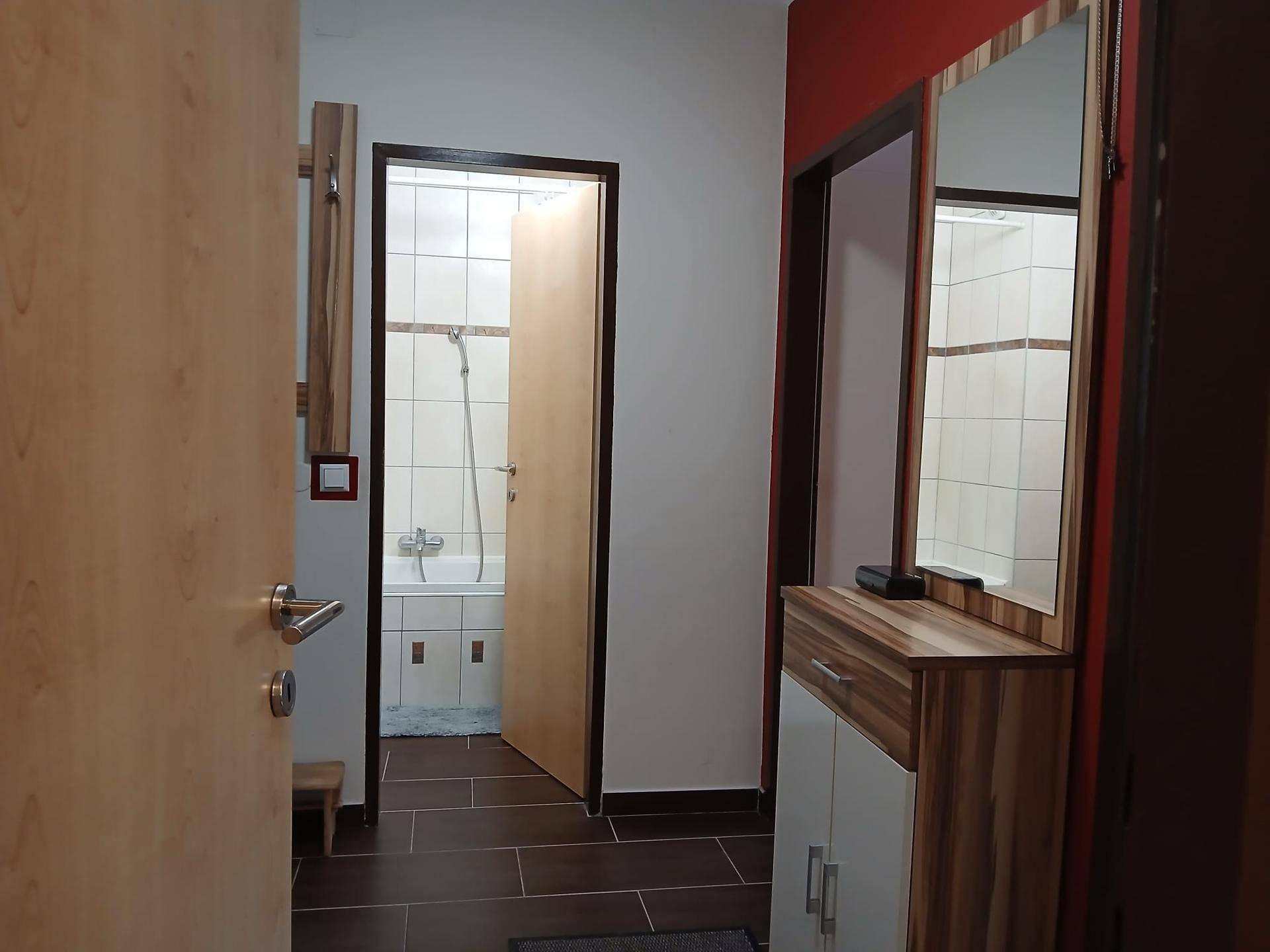 Flur mit dunklen Fliesen, einer Garderobe und einem offenen Blick in das Badezimmer. Der Bereich ist funktional gestaltet.