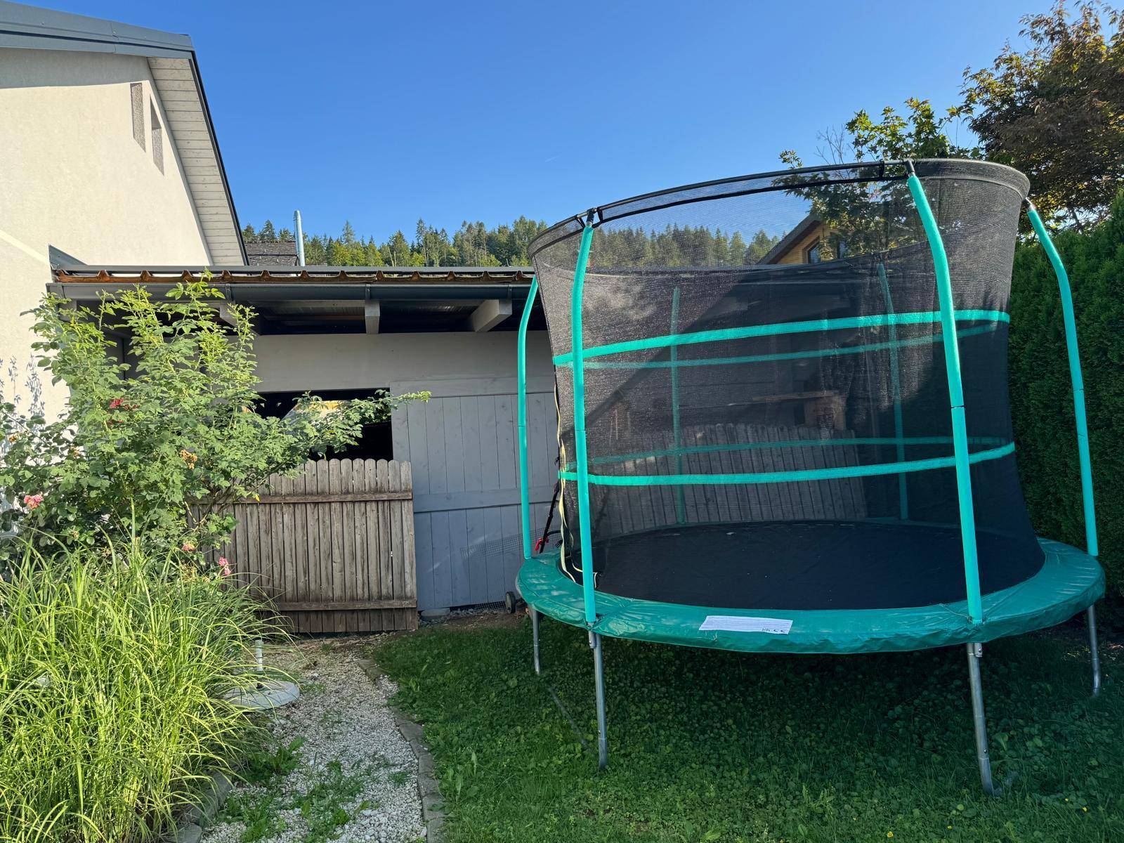 Gepflegter Gartenbereich mit großem Trampolin und Gartenhaus.
