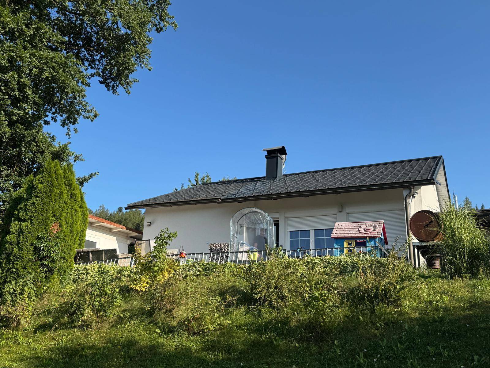 Rückansicht des Hauses mit Terrasse und Blick auf die grüne Landschaft unter blauem Himmel.