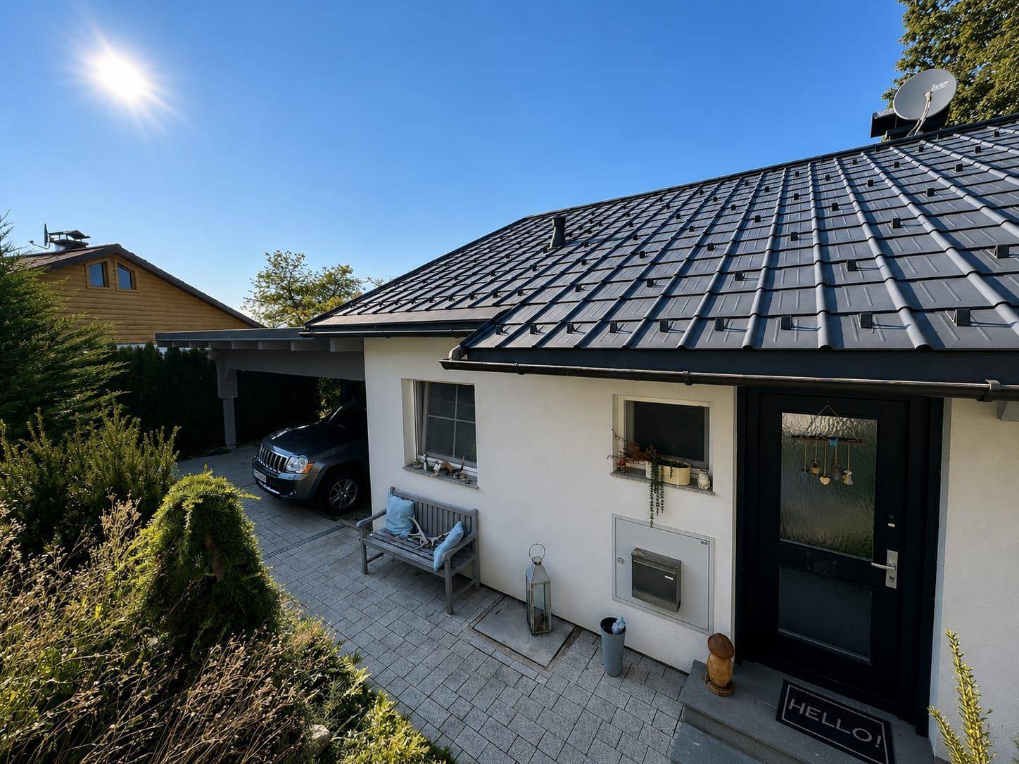 Hausfront mit Eingangsbereich, gepflastertem Weg und einem Carport auf der linken Seite.