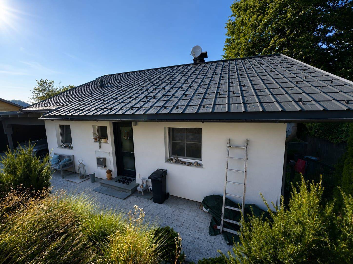 Seitliche Ansicht des Hauses mit gepflastertem Vorplatz und grüner Bepflanzung im Vordergrund.
