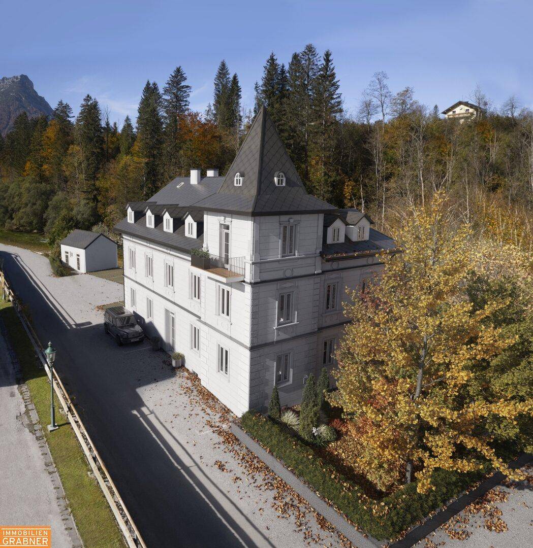 Historische Villa mit markantem Turm, umgeben von herbstlicher Landschaft und Bäumen in voller Farbe.