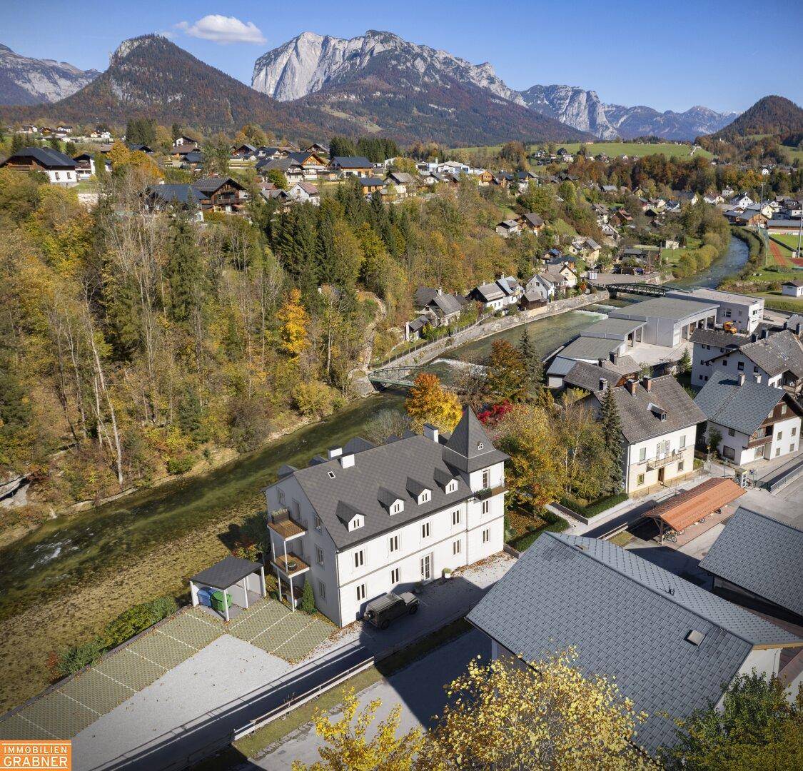 Luftaufnahme eines Anwesens in einer malerischen Berglandschaft mit Fluss und umliegenden Häusern.