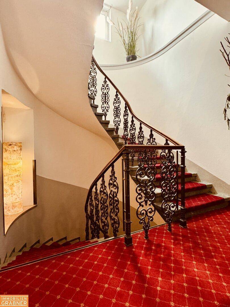 Elegante geschwungene Treppe mit rotem Teppich und kunstvollem schmiedeeisernem Geländer.