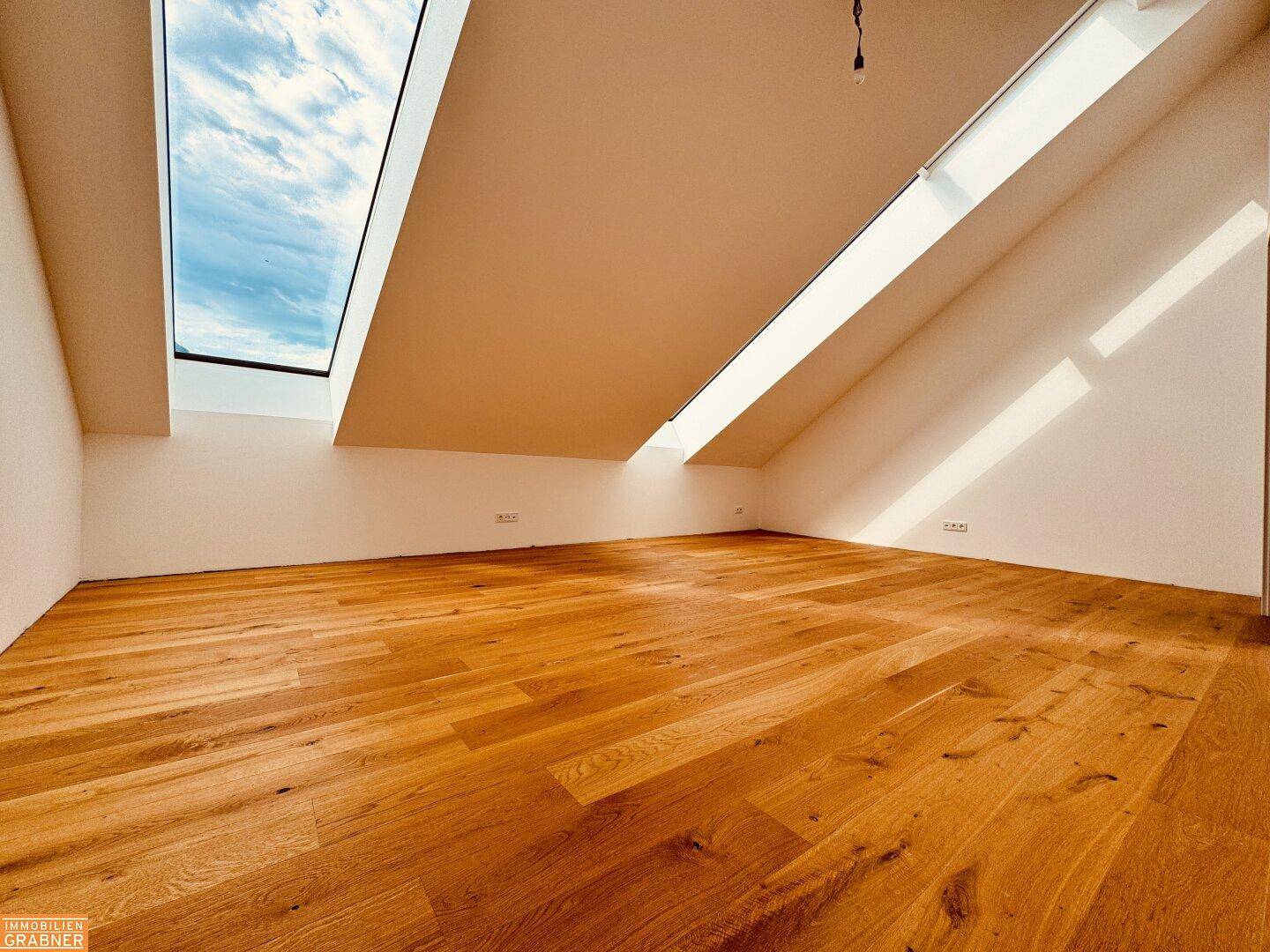 Detailansicht des hellen Holzbodens und der schrägen Dachfenster in einem leeren Raum.