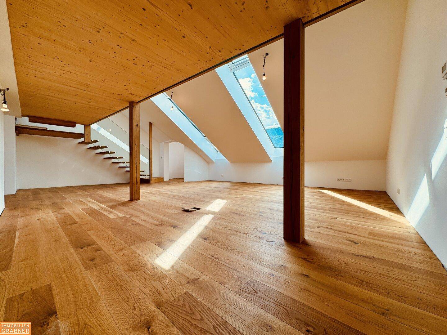 Geräumiger Dachbodenraum mit Holzboden, sichtbaren Holzbalken und einer modernen Treppe.
