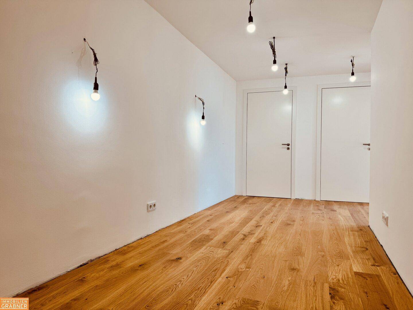 Heller Flur mit Holzboden und mehreren weißen Türen, der zu den Zimmern führt.