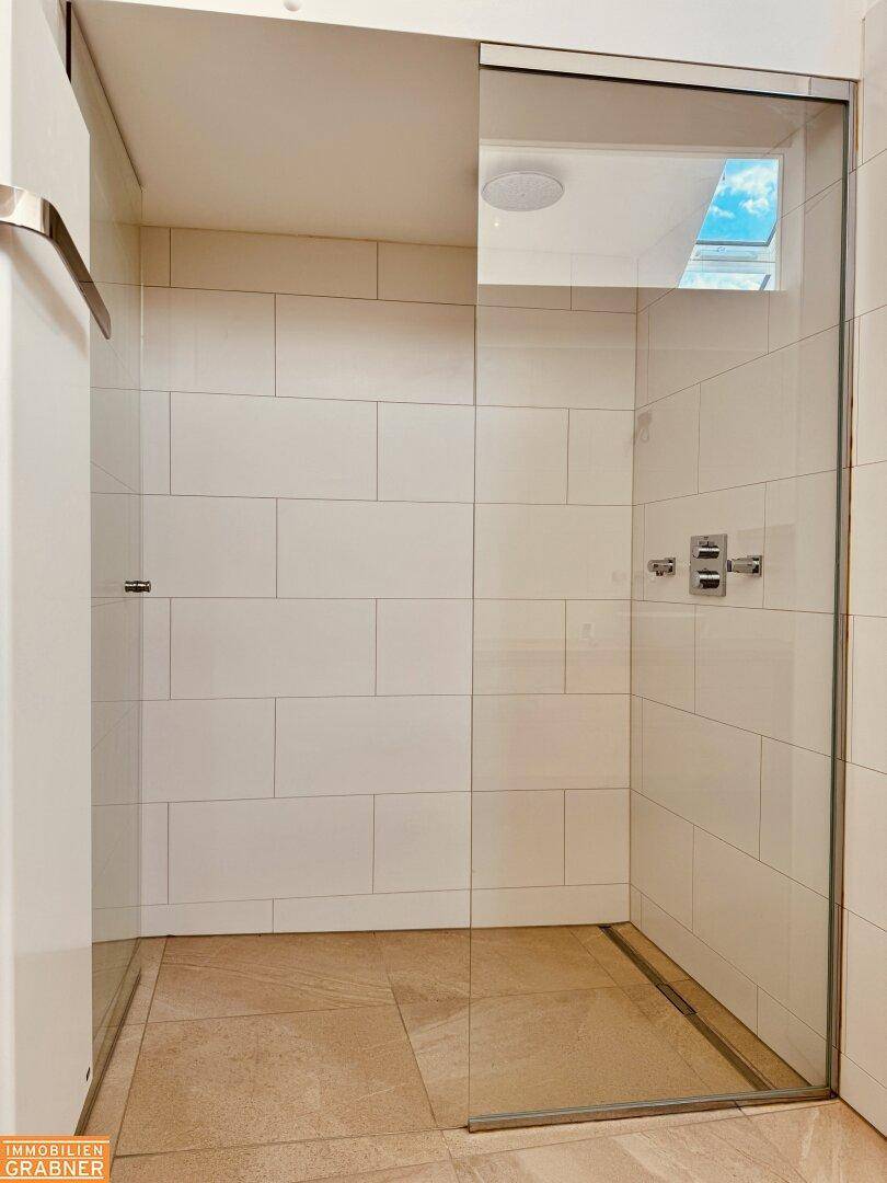 Geräumige begehbare Dusche mit Glasabtrennung und weißen Fliesen, hell durch Dachfenster.
