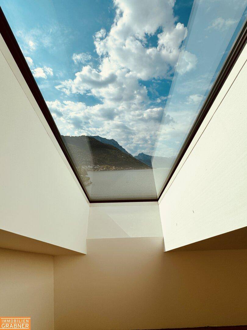 Spektakulärer Blick durch ein großes Dachfenster auf den See und die umliegenden Berge.