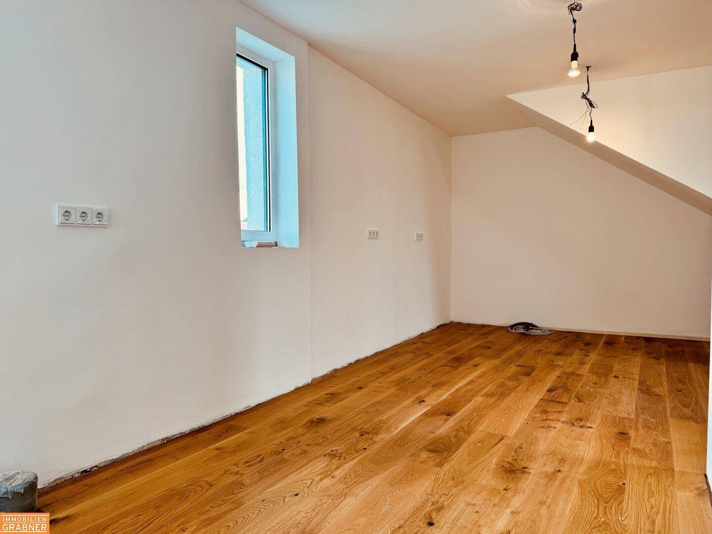 Heller Raum mit Holzboden, einem Fenster und einer Dachschräge, ideal für ein Schlafzimmer.