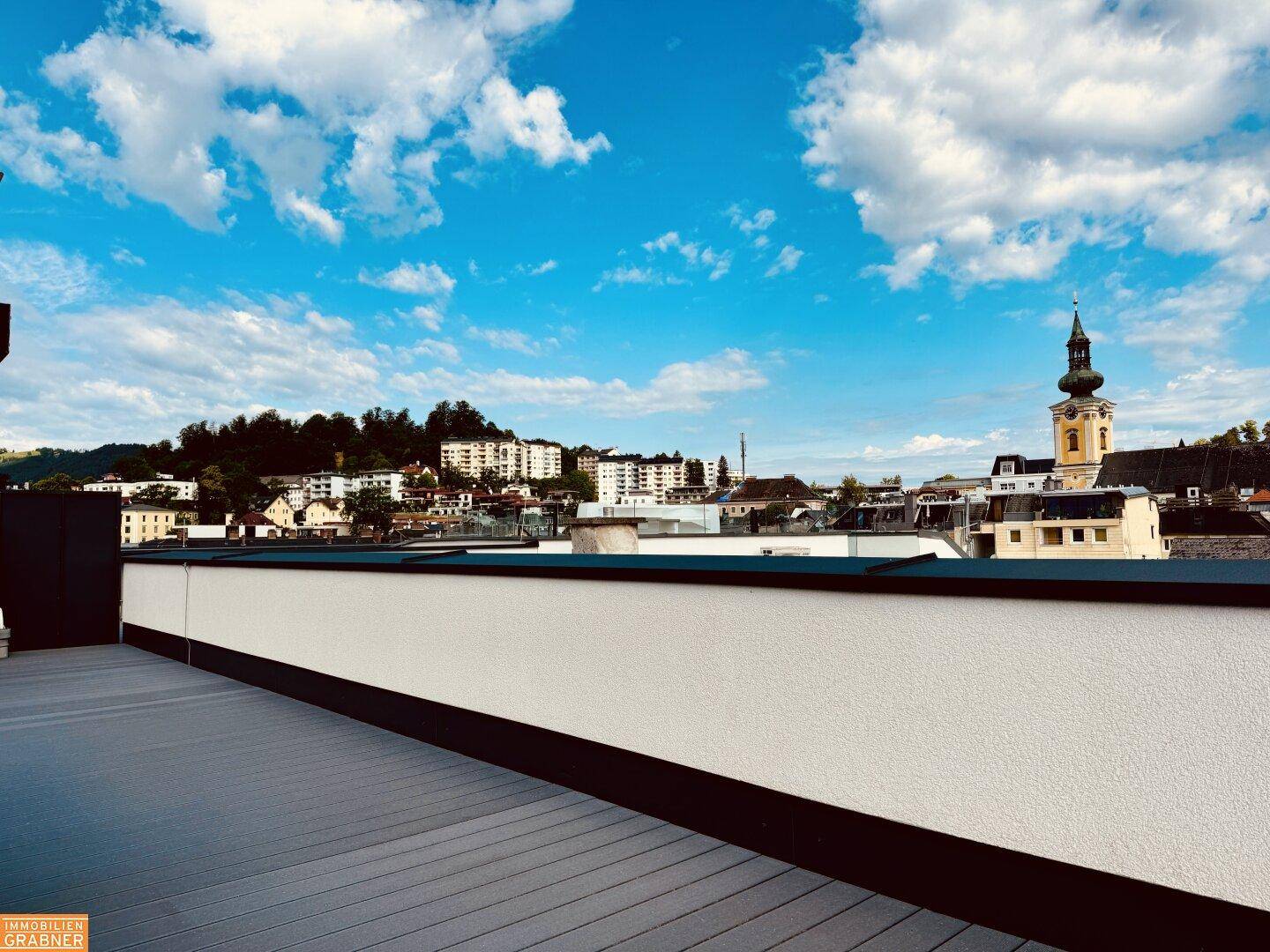 Geräumige Dachterrasse mit modernem Bodenbelag und Blick über die Stadt und die Hügel.