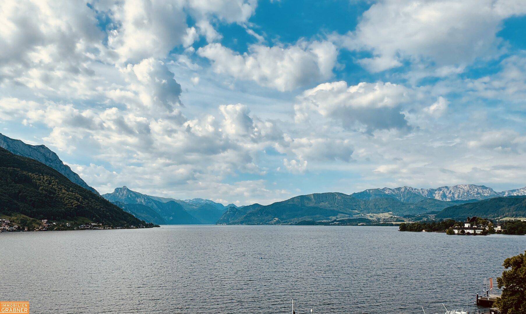 Weitläufiger Blick auf den ruhigen See, umgeben von majestätischen Bergen unter einem bewölkten Himmel.