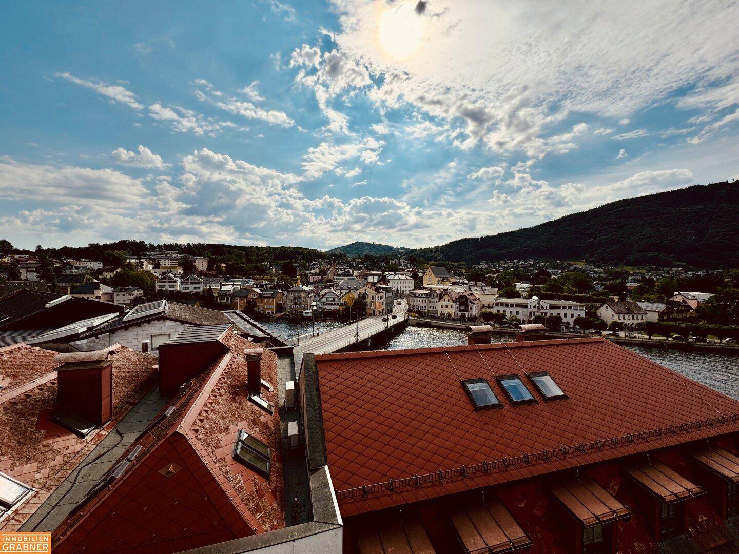 Panoramablick über die Stadt mit Dächern, einer Brücke und dem Fluss unter blauem Himmel.