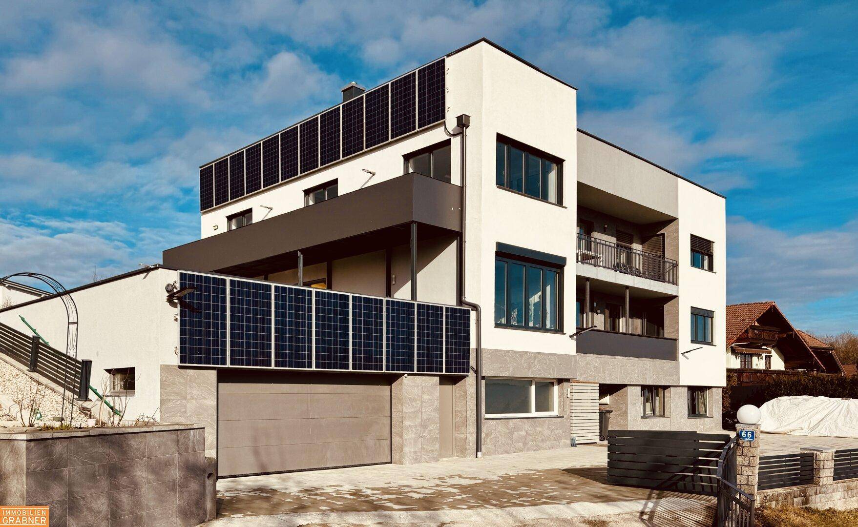 Modernes Mehrfamilienhaus mit integrierter Garage, Photovoltaikanlagen und zeitgenössischer Architektur.