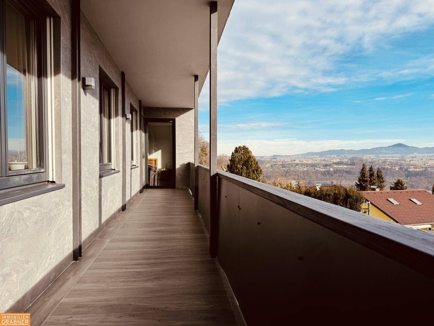 Langer Balkon mit Holzboden und weitem Blick über die Landschaft und entfernte Berge.