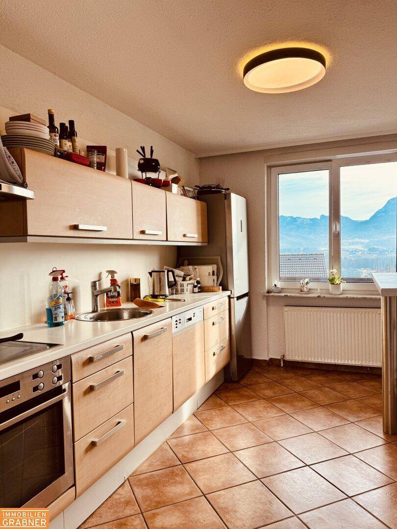 Funktionale Küche mit hellen Holzschränken, Einbaugeräten und Fenster mit Bergblick.