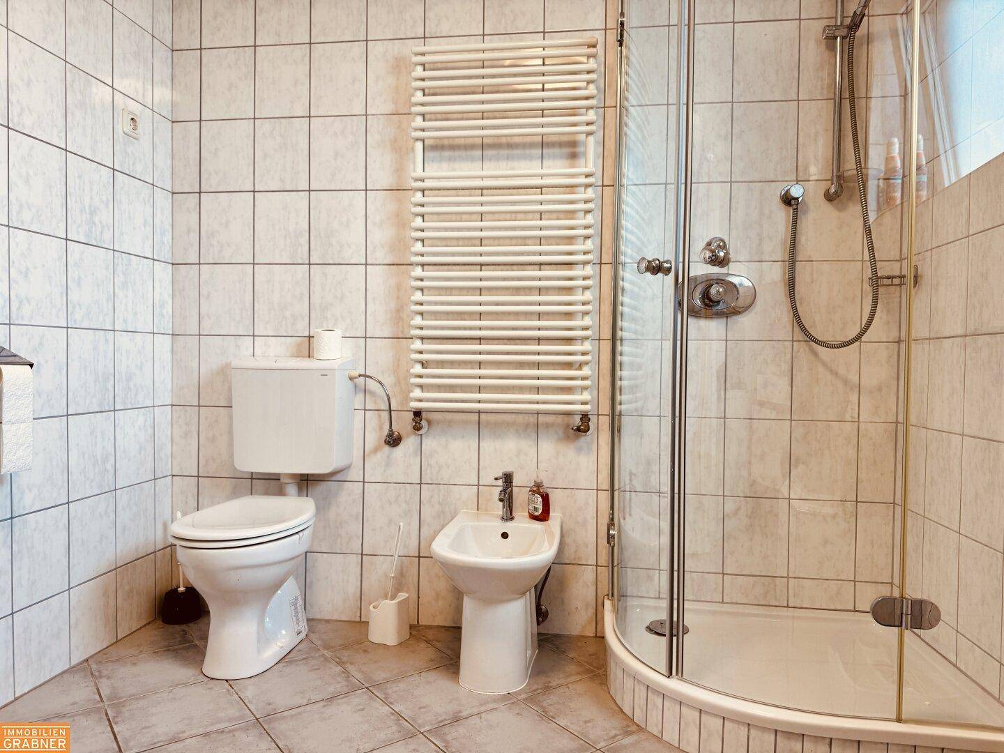 Gefliestes Badezimmer mit Dusche, WC, Bidet und beheiztem Handtuchhalter.