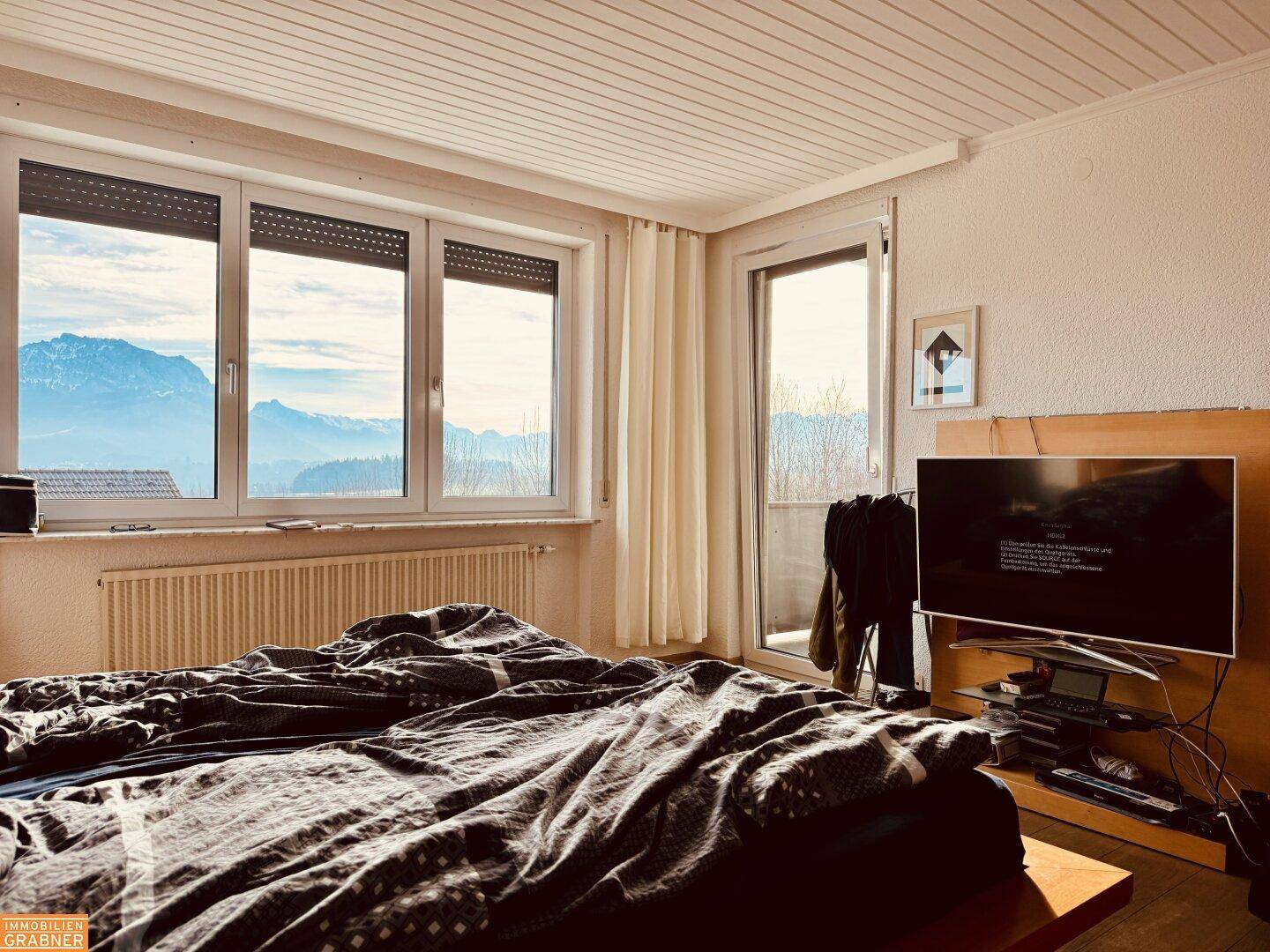 Schlafzimmer mit Doppelbett, Holzboden und Zugang zum Balkon mit Bergblick.