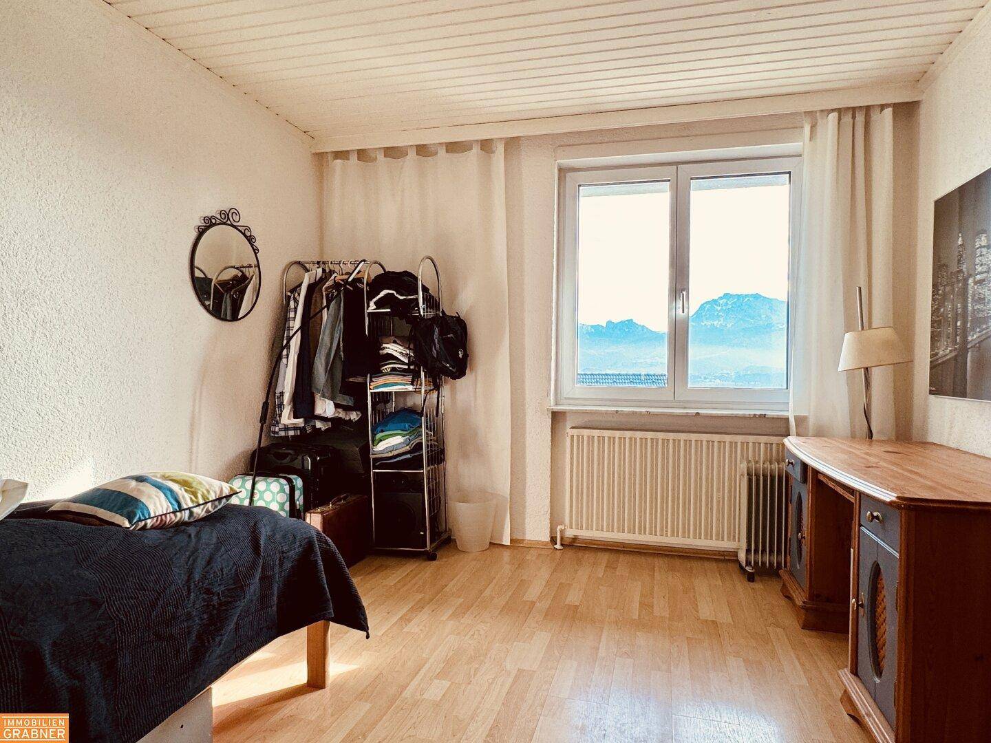 Schlafzimmer mit Holzboden, großem Fenster und Blick auf die umliegende Landschaft.