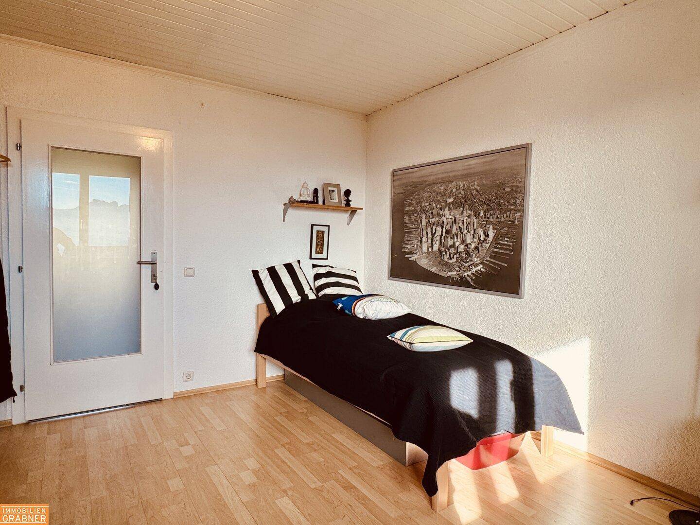 Helles Schlafzimmer mit Holzboden, Einzelbett und Blick auf die umliegende Landschaft.