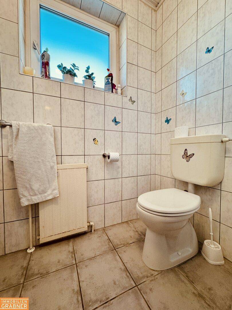 Kleines WC mit Fenster, Fliesen an Wänden und Boden sowie Schmetterlingsdekoration.