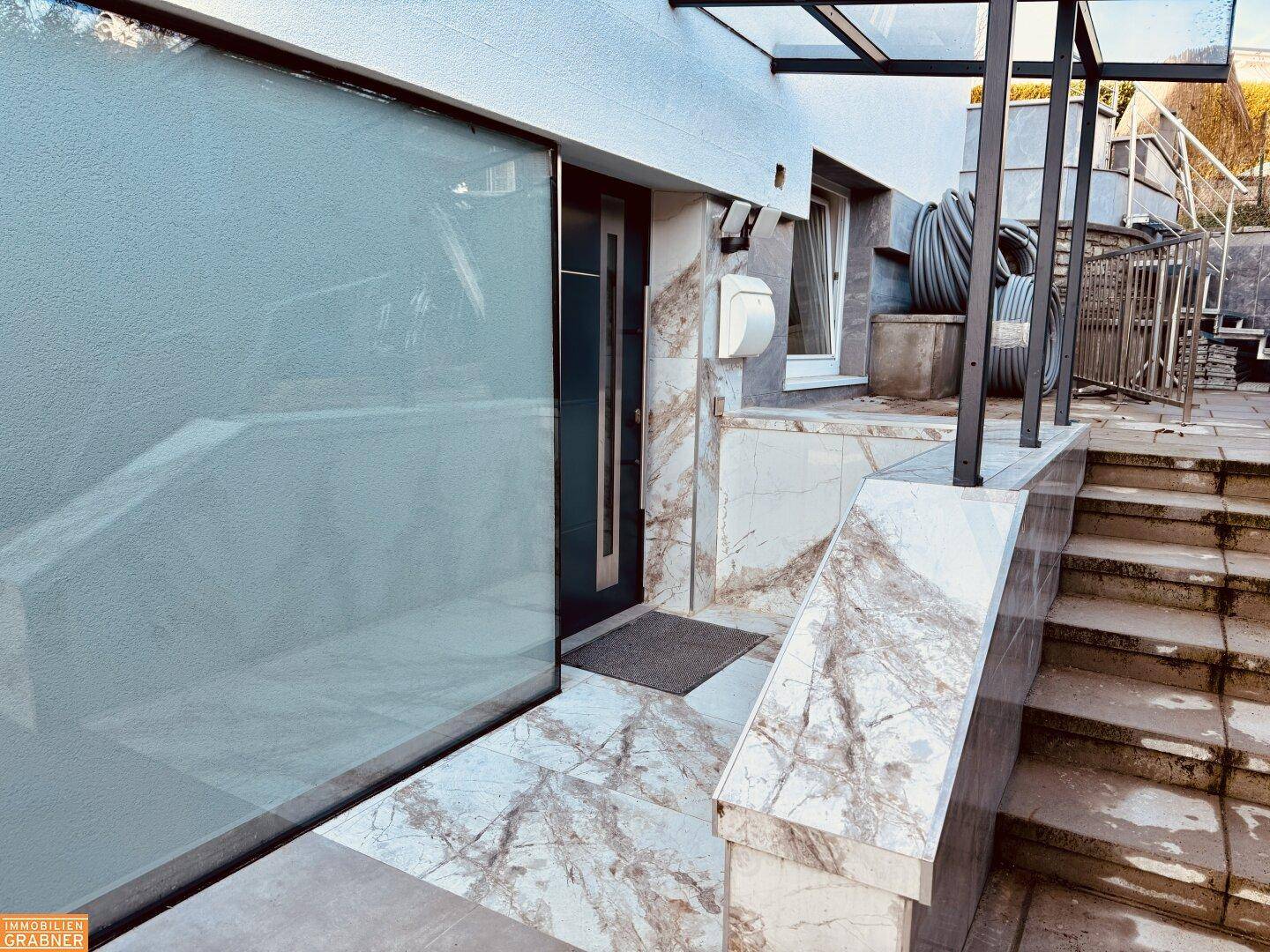 Eingangsbereich des Gebäudes mit Marmoroptik-Treppe und moderner Tür.