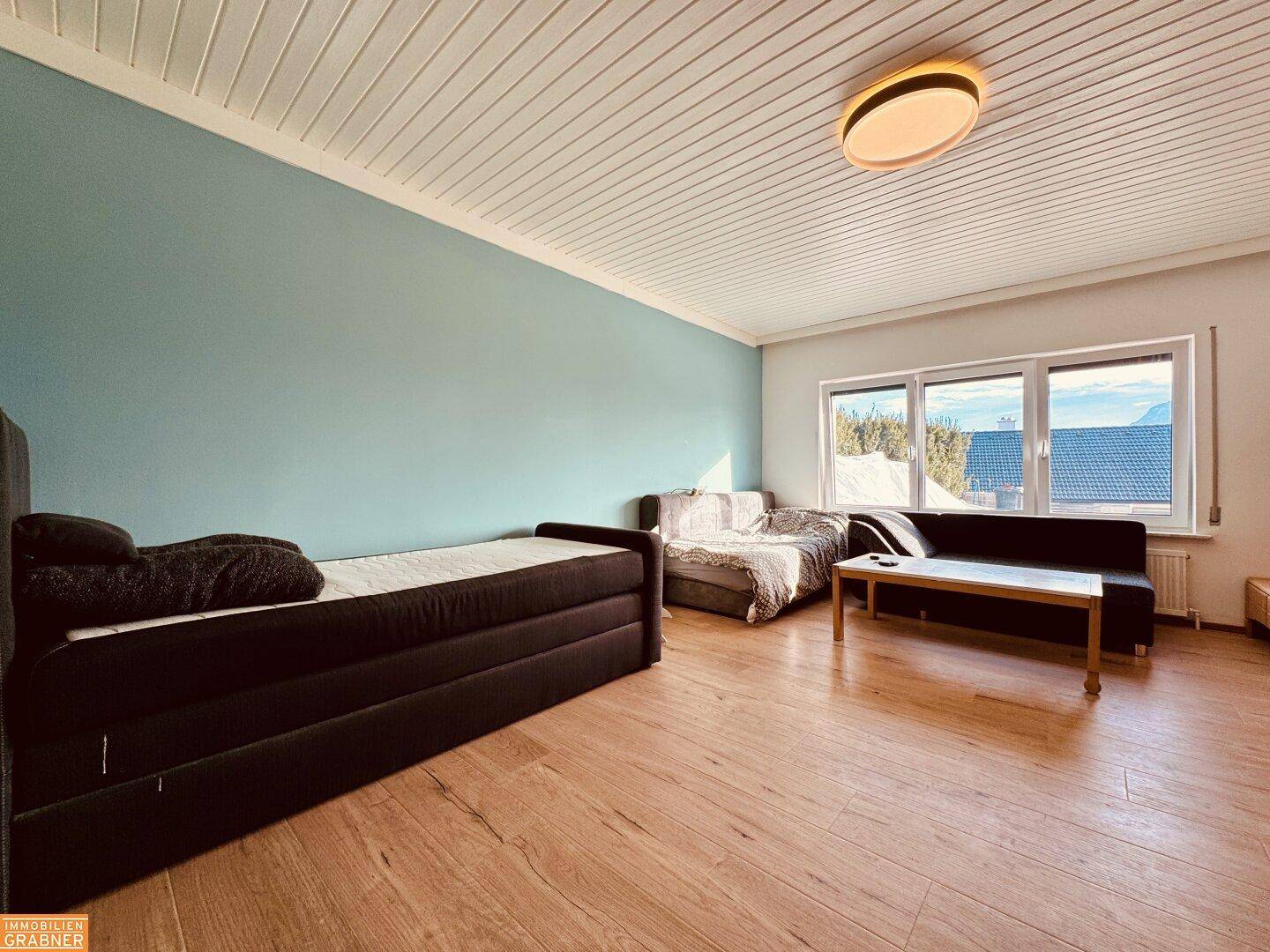 Gemütliches Zimmer mit Holzboden, blauer Wand und Blick ins Grüne.