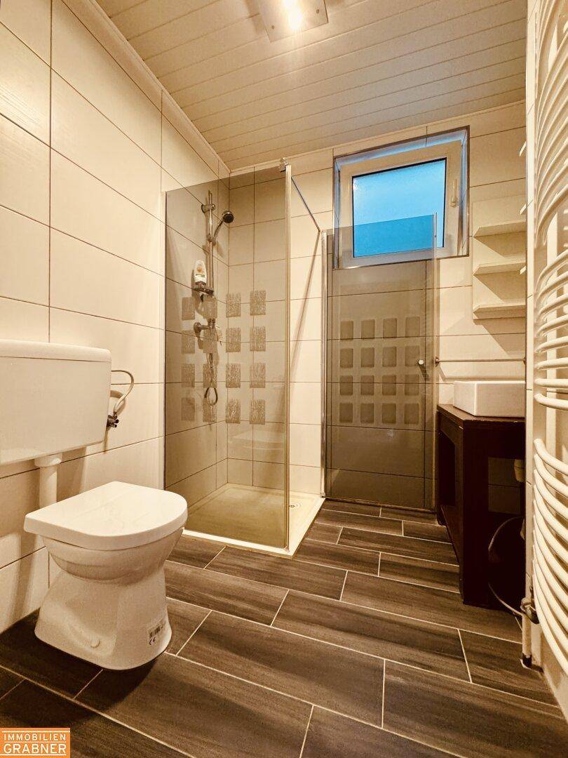 Modernes Badezimmer mit Duschkabine, WC, Fenster und Handtuchheizkörper.