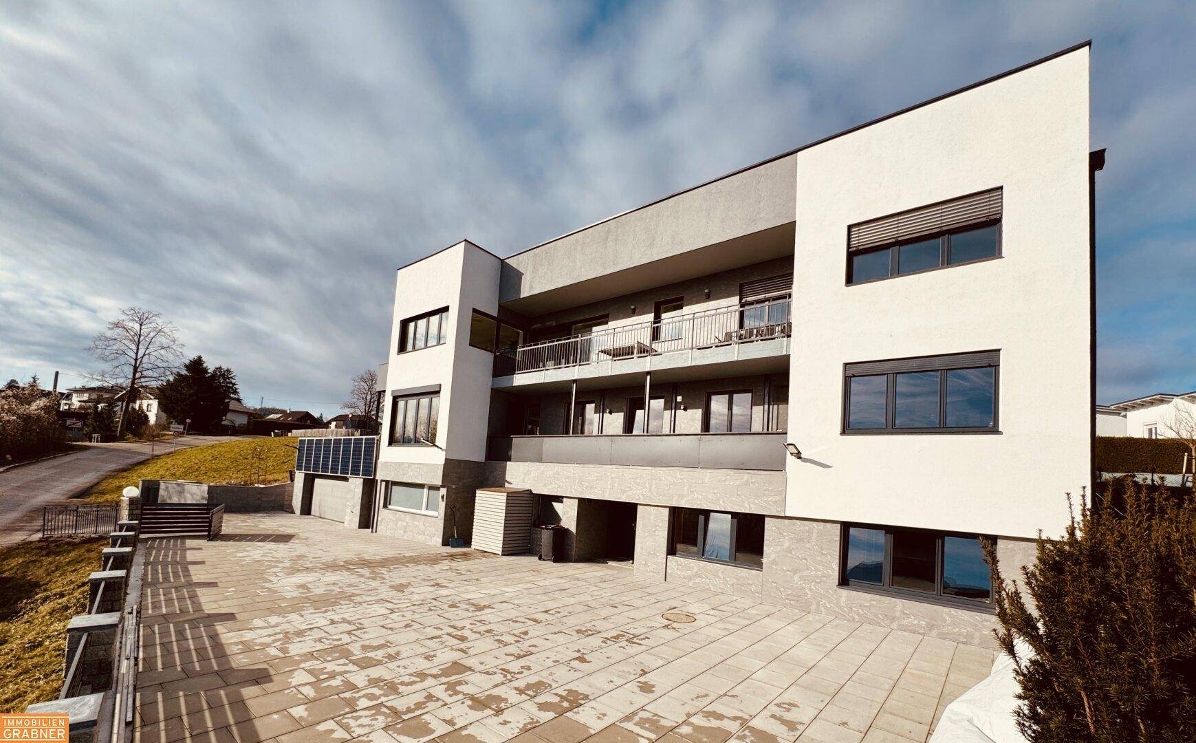 Modernes Mehrfamilienhaus mit Balkonen, gepflastertem Vorplatz und Photovoltaikanlage.