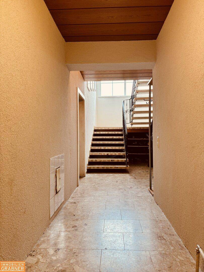 Langer Flur mit Fliesenboden und Treppe, die in die oberen Stockwerke führt.