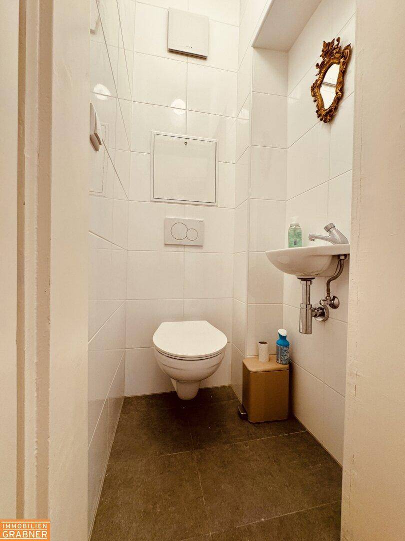 Kleines Gäste-WC mit weißen Fliesen, wandhängendem WC und kleinem Waschbecken.