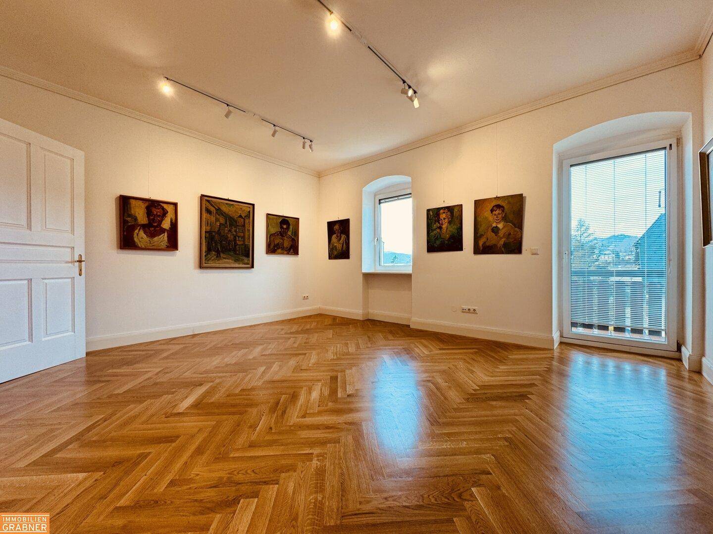 Heller Wohnraum mit Fischgrätparkett, Kunstwerken und Zugang zu einem französischen Balkon.