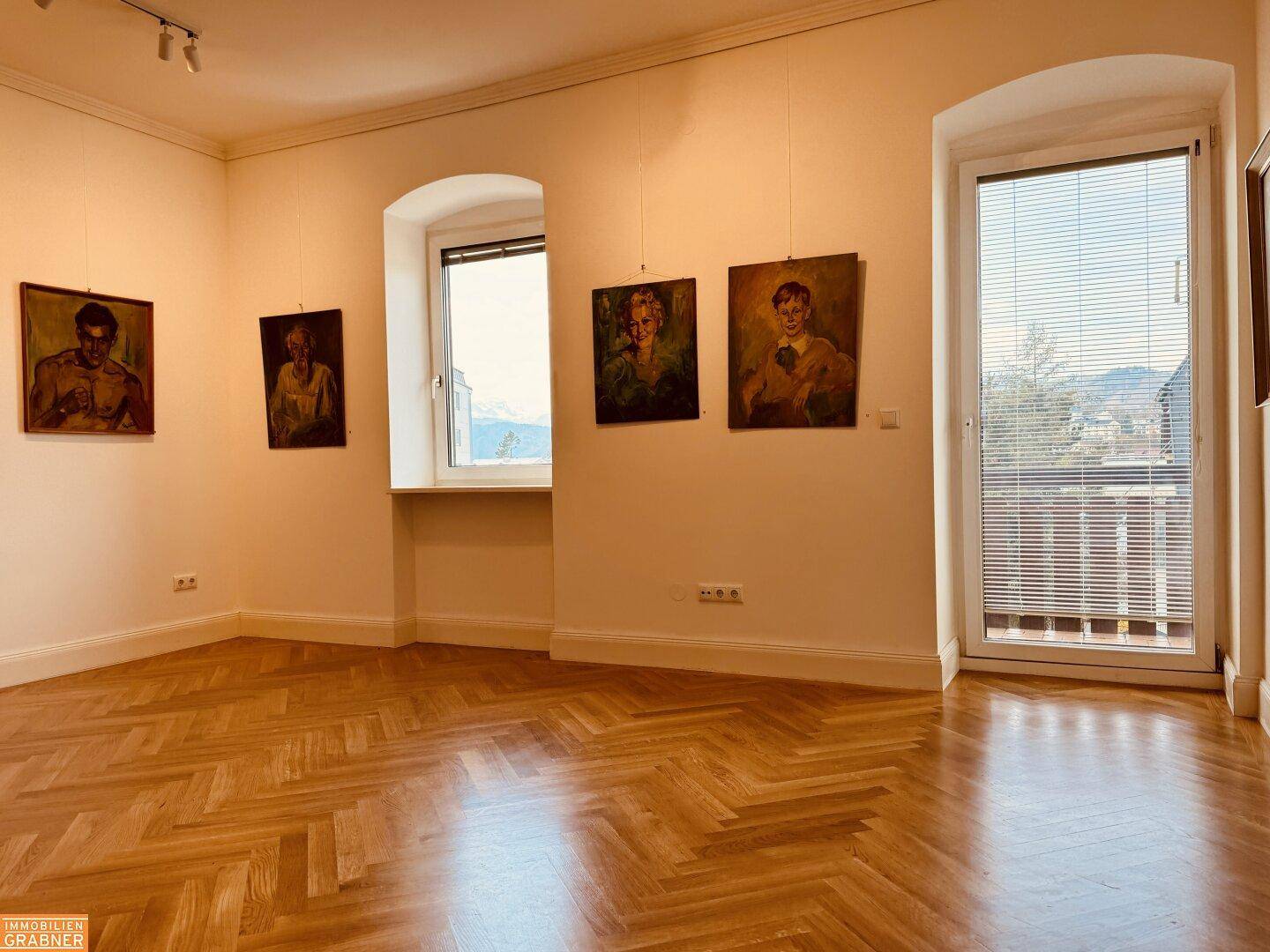 Lichtdurchfluteter Raum mit Fischgrätparkett, Kunstwerken und Blick nach draußen.