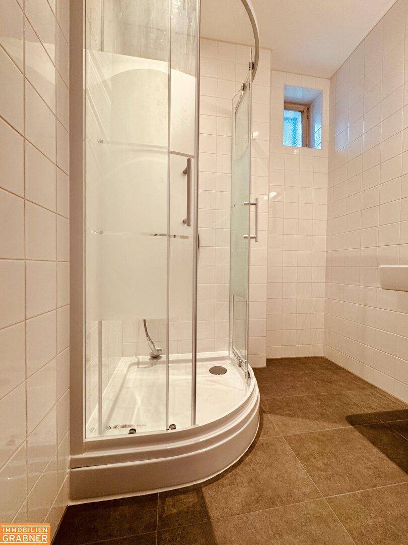 Badezimmer mit Duschkabine, weißen Fliesen und dunklem Boden.