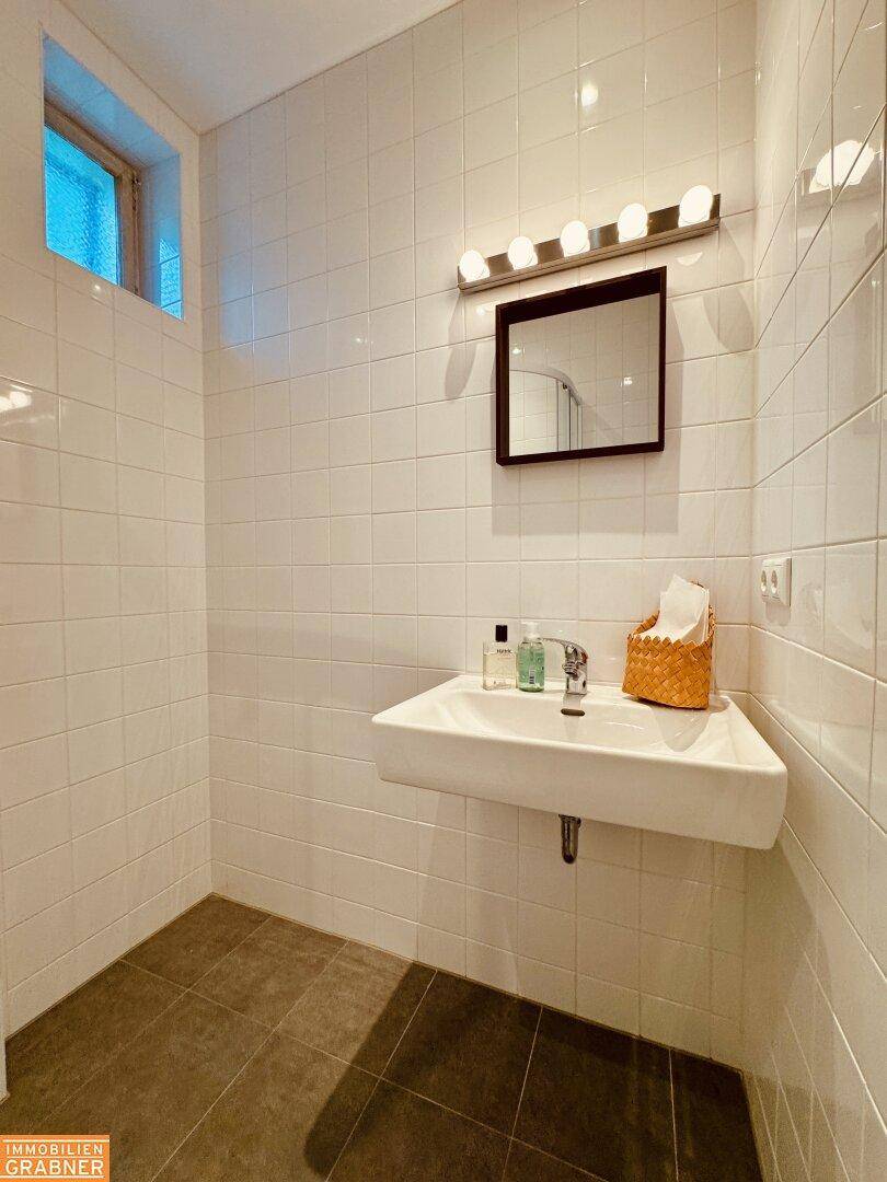 Badezimmer mit Waschbecken, Spiegel und weißen Fliesen, gut beleuchtet.