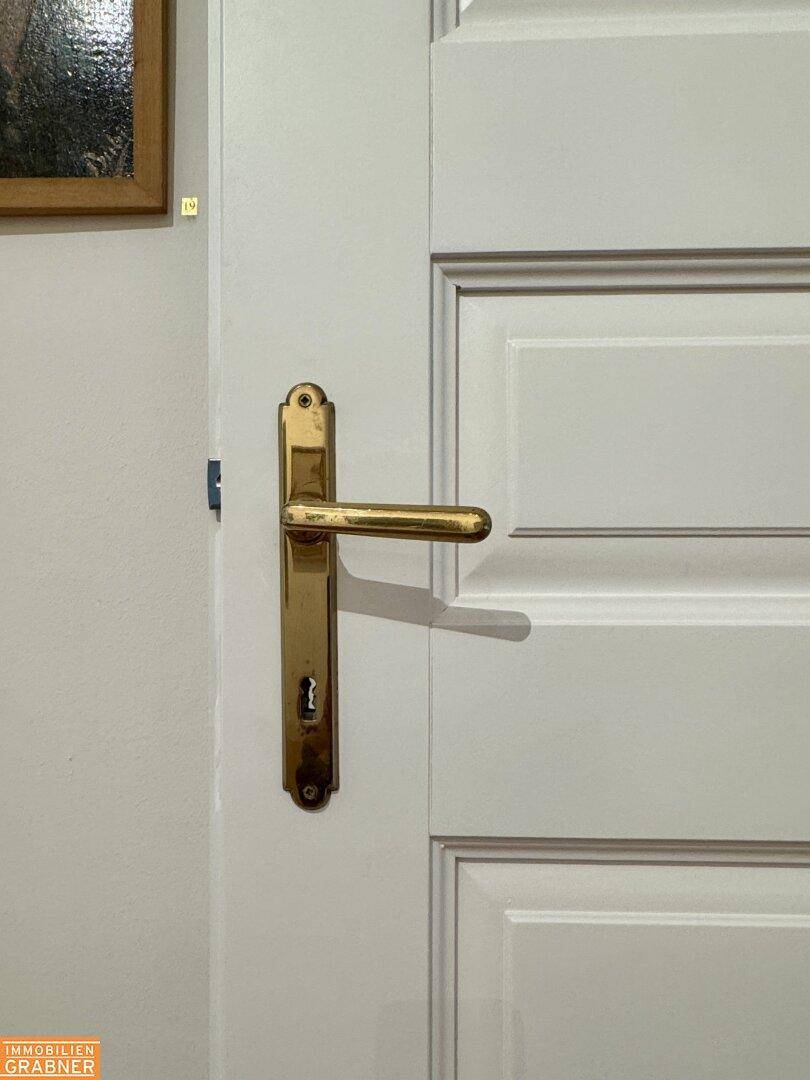 Detailaufnahme einer weißen Tür mit goldener Klinke und klassischem Design.