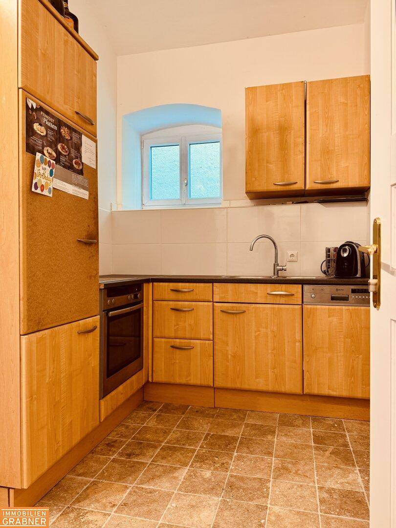 Funktionale Küche mit Holzschränken, Einbaugeräten und einem Fenster.