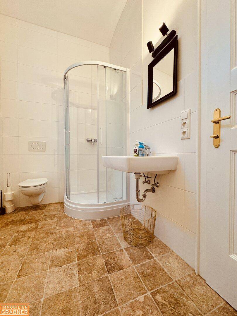 Badezimmer mit Duschkabine, WC und Waschbecken, gefliestem Boden.